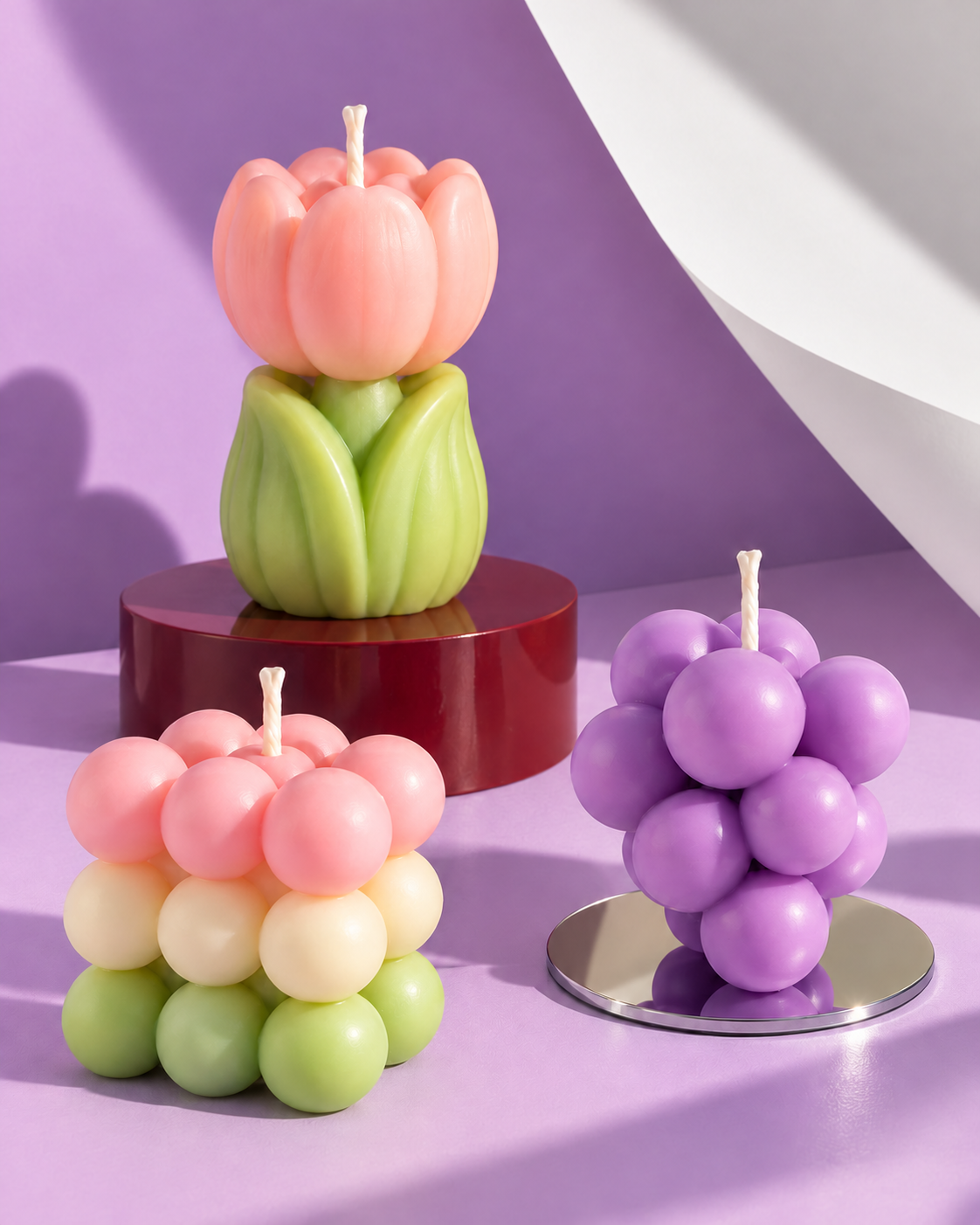 Pink tulip, purple grapes and a pastel bubble candle in an art-directed lilac studio scene